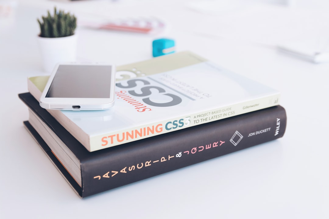 Smartphone resting on two CSS books stacked on a white desk, with a small potted plant in the background.