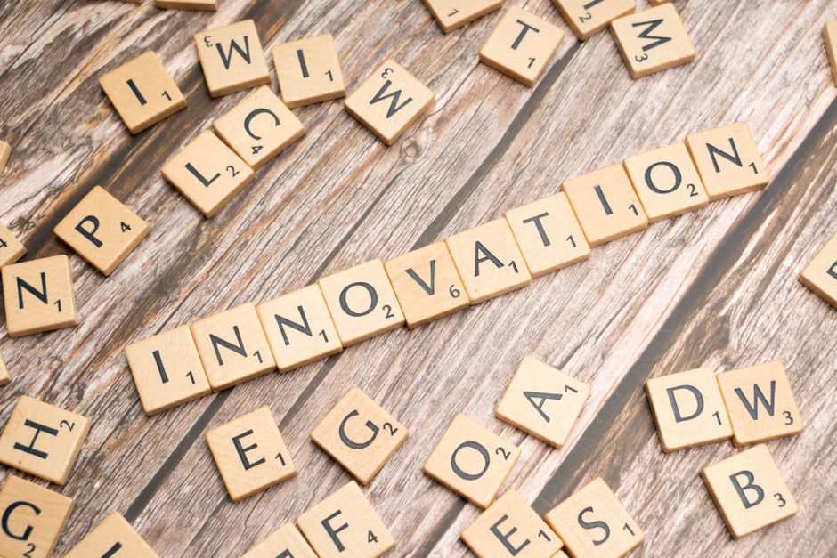 Scrabble tiles spell 'INNOVATION' on a wooden table with scattered letters around it.