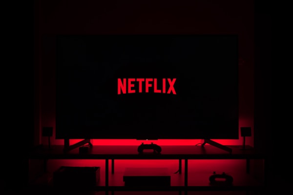 Flat-screen TV on a stand displays the Netflix logo in red, in a dark living room with red backlighting.